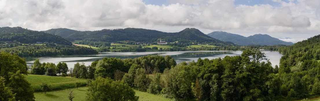 Aussicht auf den St. Georgener See mit grünen Wäldern und Bergen unter bewölktem Himmel